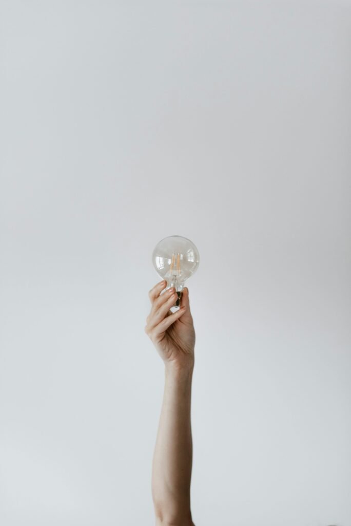 A hand raises a light bulb against a soft gray background, symbolizing creativity and ideas.